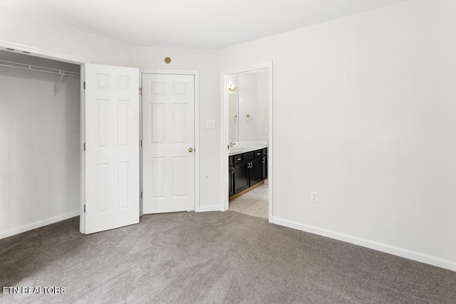 unfurnished bedroom with baseboards, carpet flooring, ensuite bathroom, a closet, and a sink