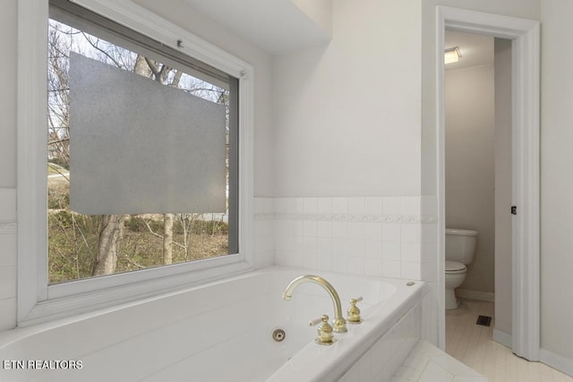 bathroom with a jetted tub, toilet, a healthy amount of sunlight, and baseboards