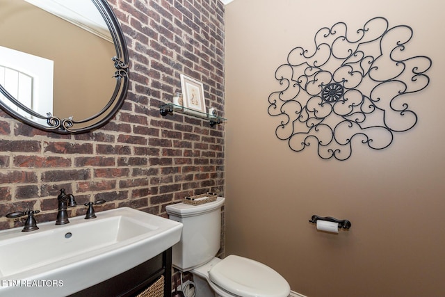 half bathroom with brick wall, toilet, and vanity