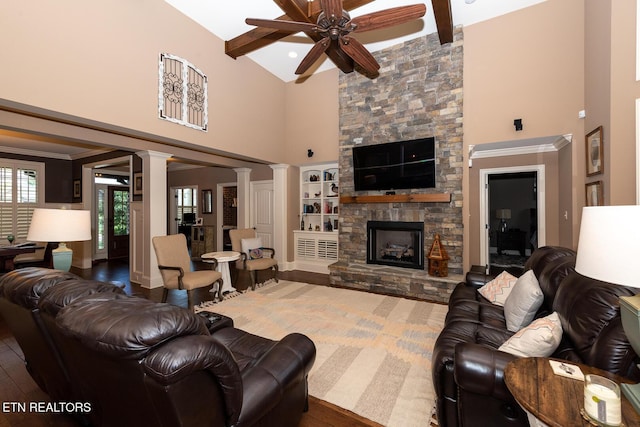 living area featuring wood finished floors, ornate columns, beam ceiling, a fireplace, and a towering ceiling