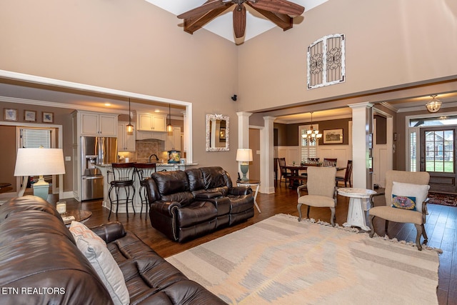 living room with ceiling fan with notable chandelier, crown molding, dark wood-style flooring, and ornate columns