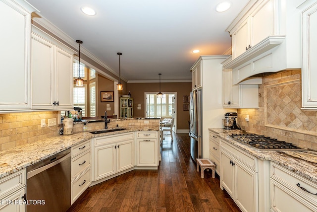 kitchen featuring dark wood-type flooring, ornamental molding, appliances with stainless steel finishes, a peninsula, and a sink