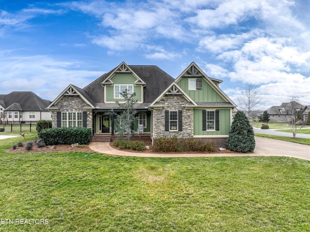 craftsman inspired home featuring stone siding, board and batten siding, a front lawn, and fence