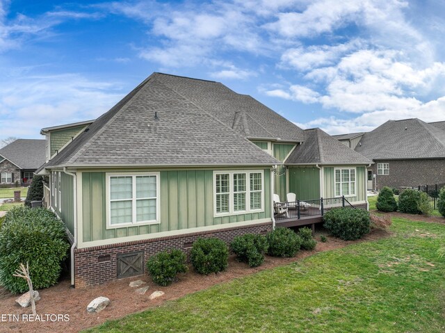 back of house featuring brick siding, a shingled roof, a deck, a lawn, and board and batten siding