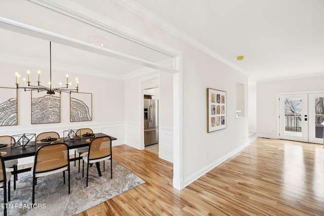 dining room with light wood-style flooring, ornamental molding, french doors, wainscoting, and a notable chandelier