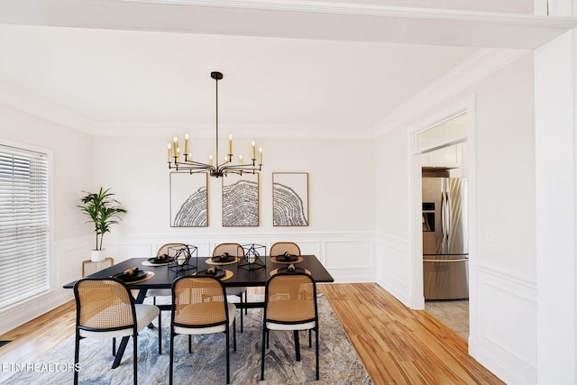 dining area featuring a decorative wall, an inviting chandelier, crown molding, and light wood finished floors