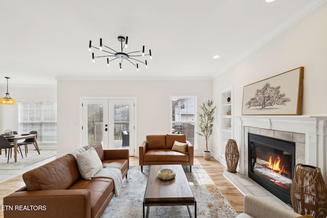 living room featuring built in features, light wood-style flooring, a tiled fireplace, and crown molding