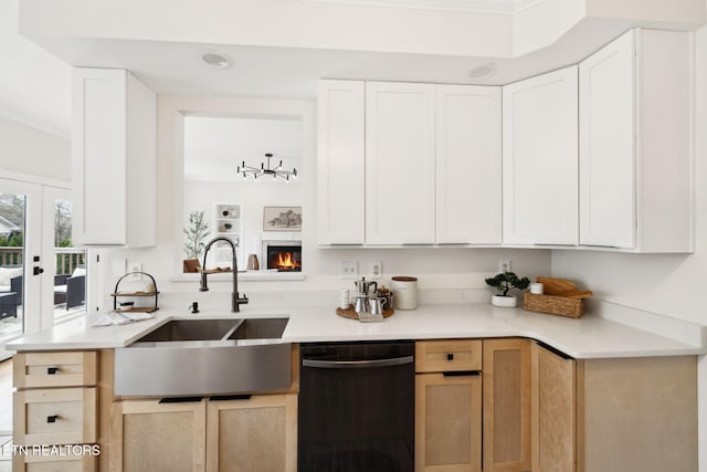 kitchen featuring crown molding, dishwasher, light countertops, a warm lit fireplace, and a sink