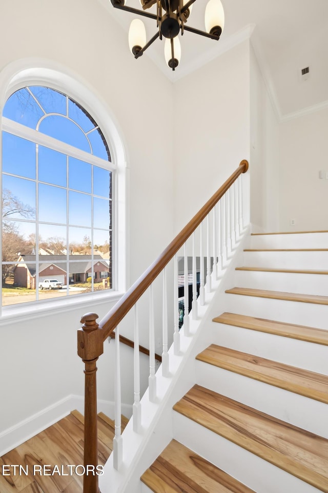 staircase with baseboards, wood finished floors, visible vents, and ornamental molding