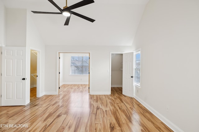 unfurnished bedroom featuring a closet, high vaulted ceiling, light wood-type flooring, and a walk in closet