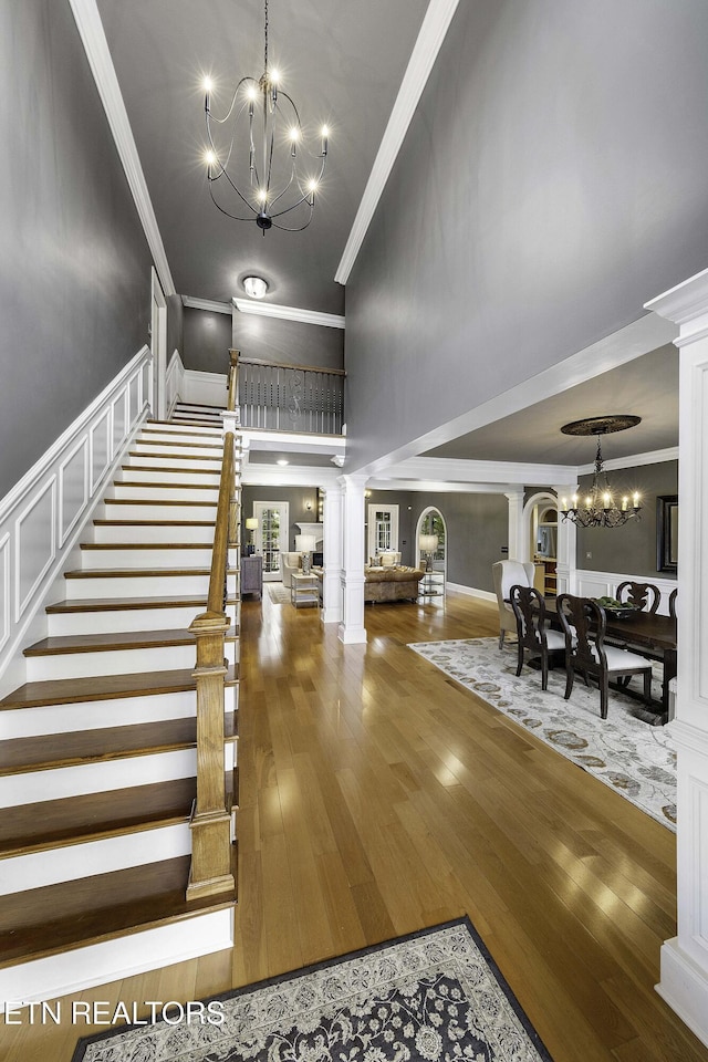 stairs with a notable chandelier, crown molding, and decorative columns