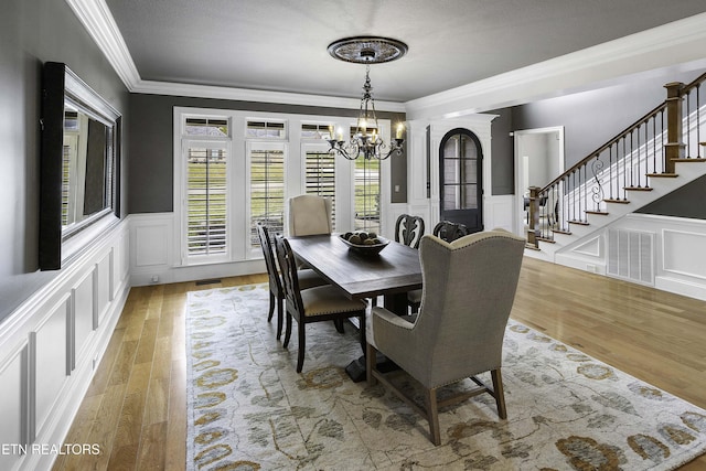 dining room with crown molding, a chandelier, light wood-type flooring, stairs, and a decorative wall