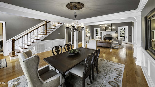 dining space with ornamental molding, wood finished floors, stairway, a fireplace, and ornate columns