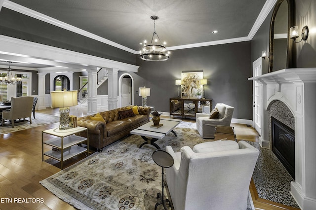 living room with wood finished floors, decorative columns, ornamental molding, a glass covered fireplace, and a chandelier