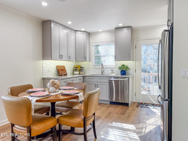 kitchen with light wood finished floors, backsplash, stainless steel appliances, and a sink