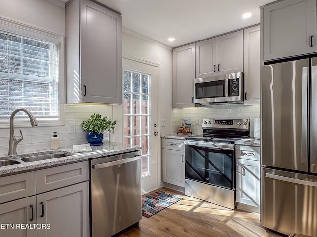 kitchen featuring tasteful backsplash, gray cabinetry, light wood-style flooring, stainless steel appliances, and a sink