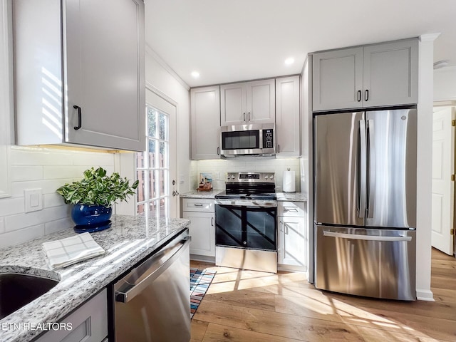 kitchen featuring gray cabinets, stainless steel appliances, light wood finished floors, decorative backsplash, and light stone countertops