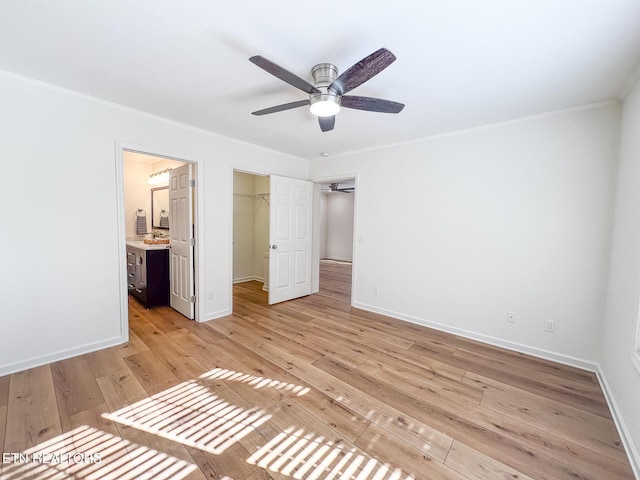 unfurnished bedroom featuring baseboards, ornamental molding, ensuite bathroom, light wood-style floors, and a closet