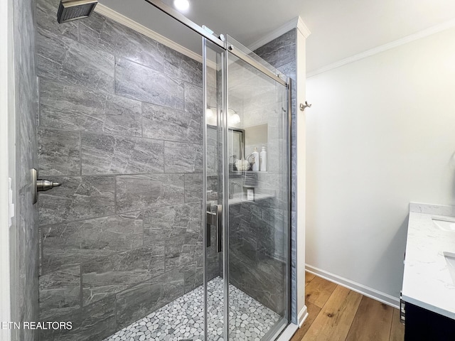 bathroom featuring vanity, wood finished floors, baseboards, ornamental molding, and a shower stall