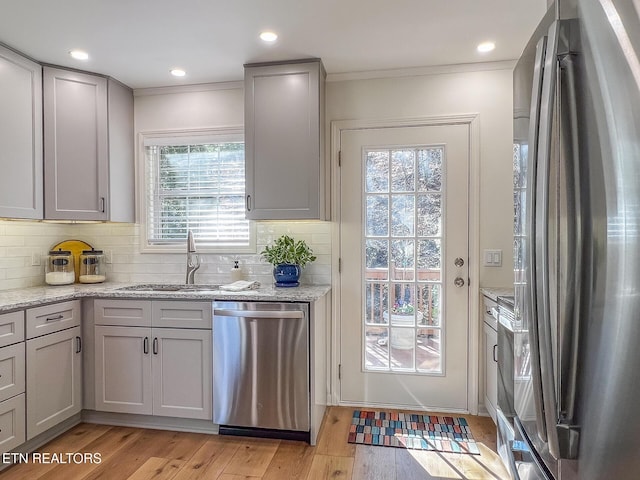 kitchen with a sink, stainless steel appliances, light wood-style floors, and ornamental molding