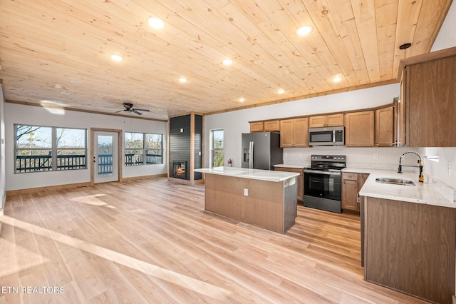 kitchen featuring a kitchen island, a sink, stainless steel appliances, open floor plan, and a large fireplace