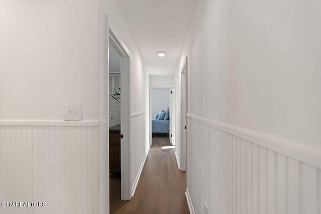 corridor featuring a wainscoted wall and dark wood-style flooring