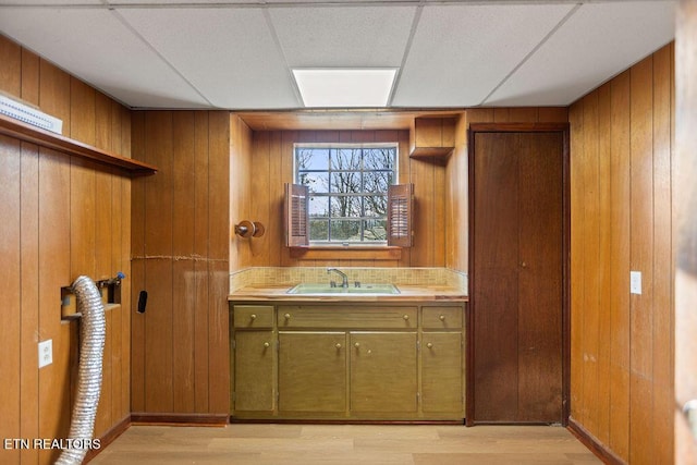 kitchen featuring a sink, light wood-style floors, wood walls, and tile countertops