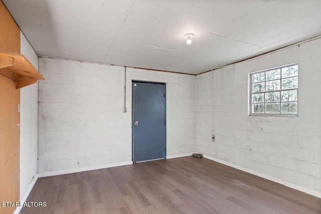 unfurnished room with concrete block wall and wood finished floors