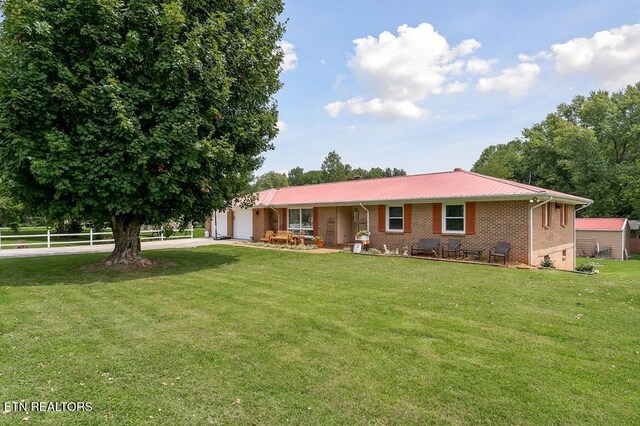 ranch-style house featuring a front yard, driveway, an attached garage, brick siding, and metal roof