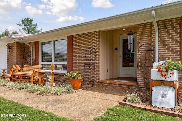 view of exterior entry with brick siding, covered porch, and a garage