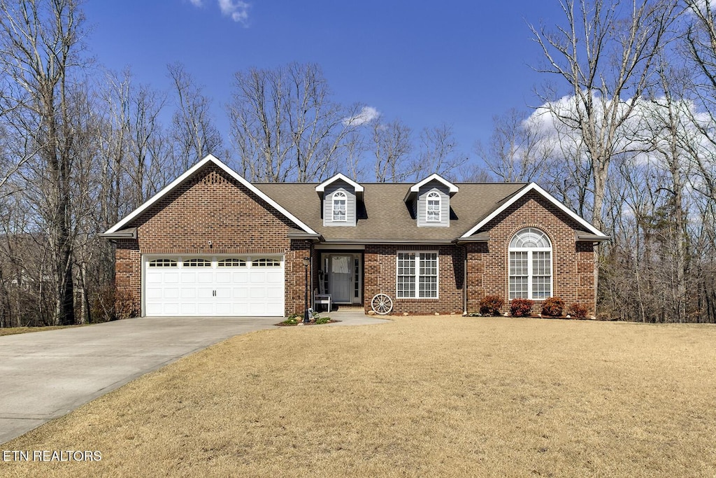 view of front of property with a shingled roof, concrete driveway, a front lawn, a garage, and brick siding