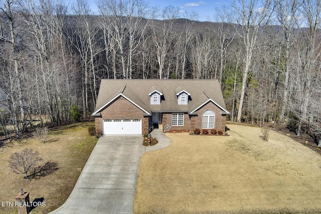 view of front of house featuring brick siding, a wooded view, driveway, and a garage