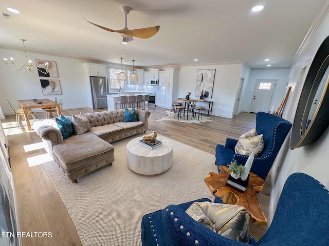 living room featuring baseboards, recessed lighting, ornamental molding, light wood-style floors, and ceiling fan with notable chandelier