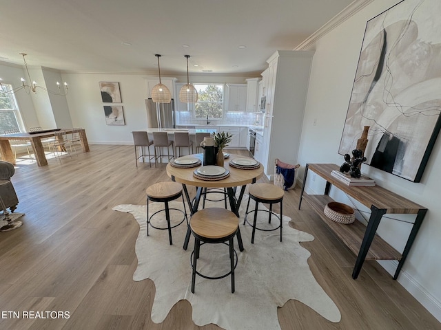 dining area featuring light wood-type flooring, baseboards, an inviting chandelier, and crown molding