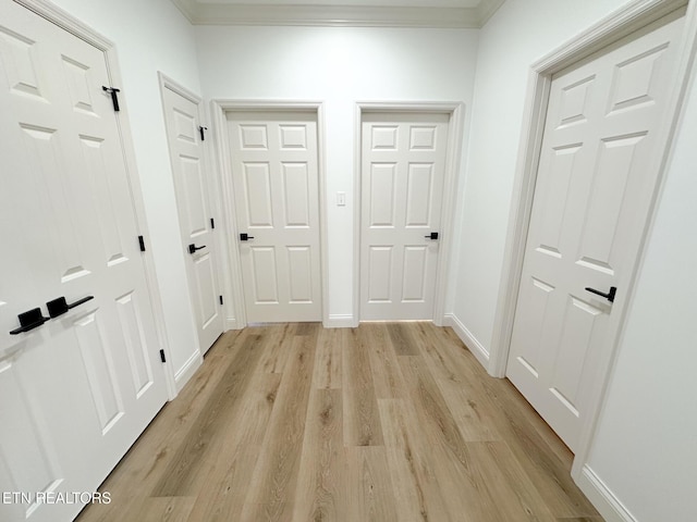 corridor featuring baseboards, crown molding, and light wood finished floors