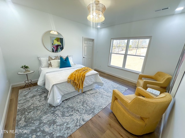 bedroom featuring visible vents, baseboards, a notable chandelier, and wood finished floors