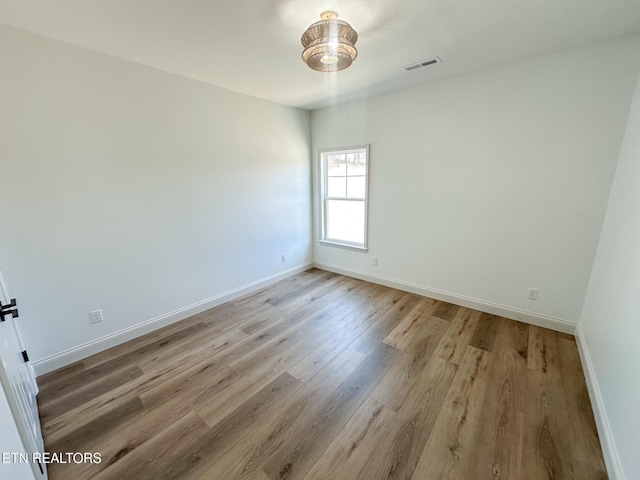 empty room with light wood finished floors, visible vents, and baseboards