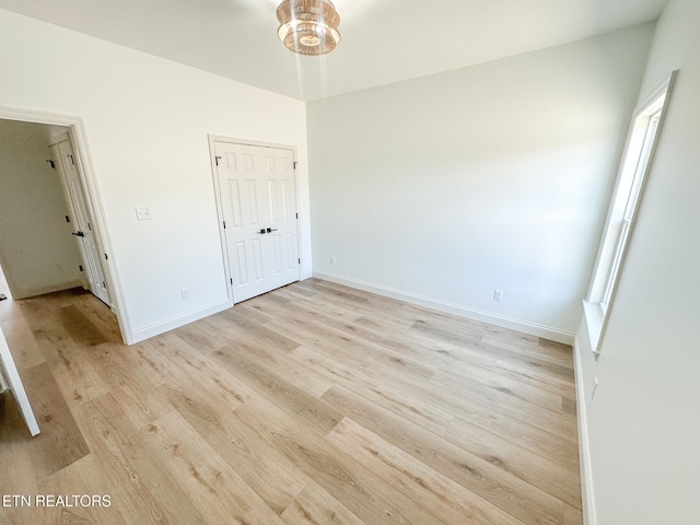 interior space with a closet, a chandelier, light wood-style flooring, and baseboards