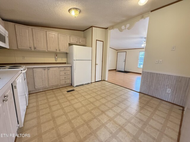 kitchen with a wainscoted wall, a textured ceiling, freestanding refrigerator, wooden walls, and light floors