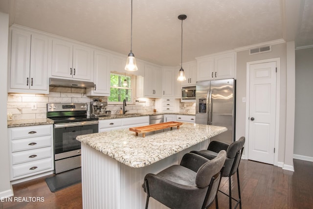 kitchen with a sink, stainless steel appliances, dark wood finished floors, under cabinet range hood, and white cabinets