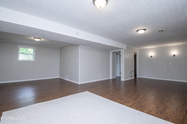 interior space featuring a textured ceiling, baseboards, wooden walls, and wood finished floors