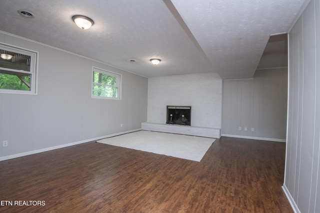 unfurnished living room with baseboards, a fireplace with raised hearth, a textured ceiling, and dark wood-type flooring