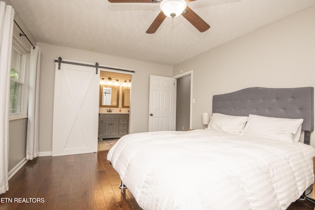 bedroom with a barn door, wood-type flooring, a ceiling fan, connected bathroom, and baseboards