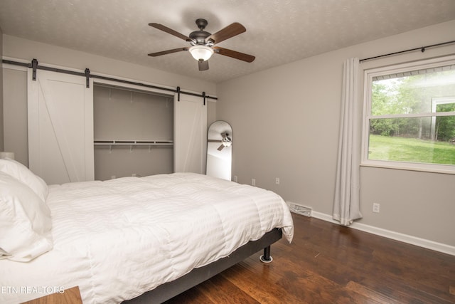 bedroom featuring baseboards, a barn door, a textured ceiling, and wood finished floors