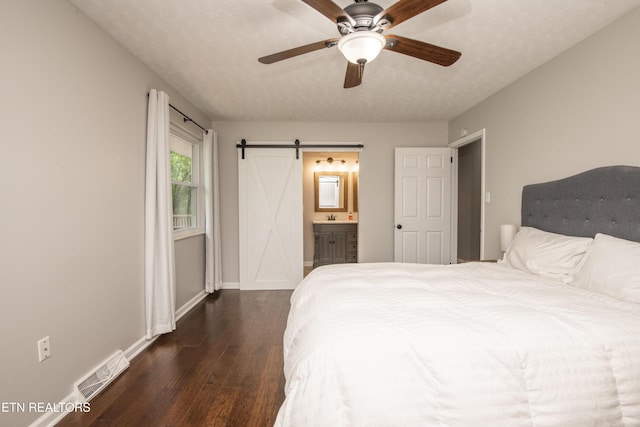 bedroom with a barn door, baseboards, ensuite bathroom, visible vents, and dark wood-style floors