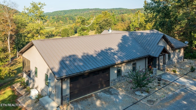 view of front of home with a forest view, metal roof, an attached garage, and a standing seam roof