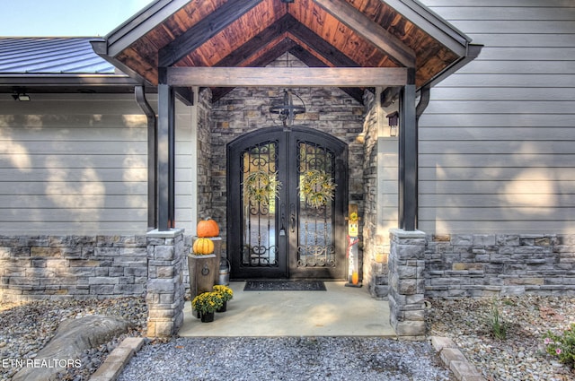 entrance to property with french doors, stone siding, metal roof, and a standing seam roof