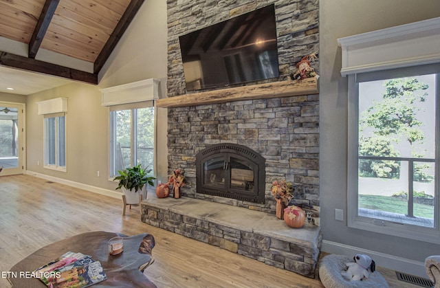 living area featuring baseboards, a stone fireplace, wood finished floors, and vaulted ceiling with beams