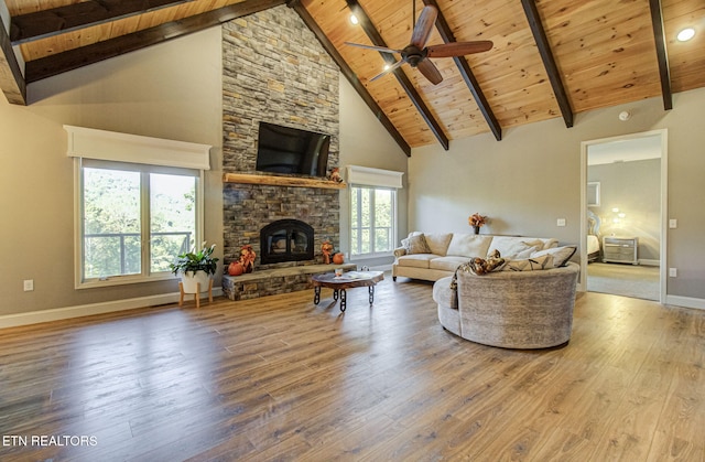 living area featuring beam ceiling, a stone fireplace, wood ceiling, and wood finished floors