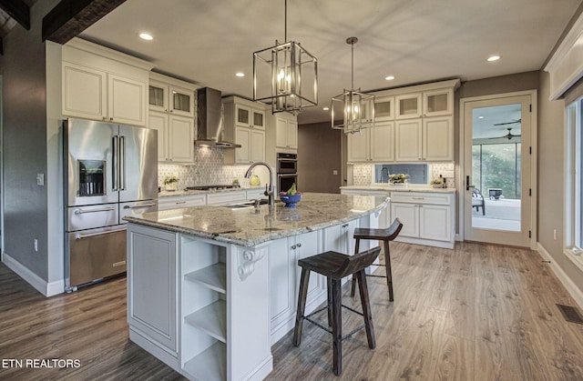 kitchen with a sink, open shelves, wood finished floors, appliances with stainless steel finishes, and wall chimney range hood